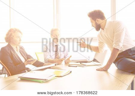 Toned of handsome businessman sitting on table in office and offering his CV to be investigated. Employees listening to man about his previous experience in huge business.