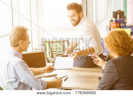 Toned of employees listening to man about his previous experience in huge business. Businessman sitting on table in office and offering his CV to be investigated.