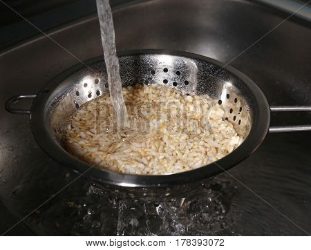 Washing brown rice with water in colander
