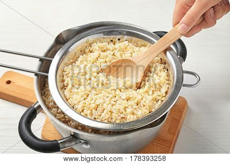 Hand with spoon stirring brown rice in colander on kitchen table