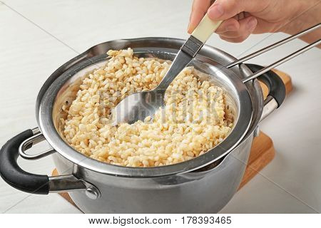 Hand with spoon stirring brown rice in colander on kitchen table