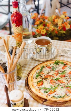 Pizza with cheese, tomato and meat, with cup of tee on served table with plaid tablecloth