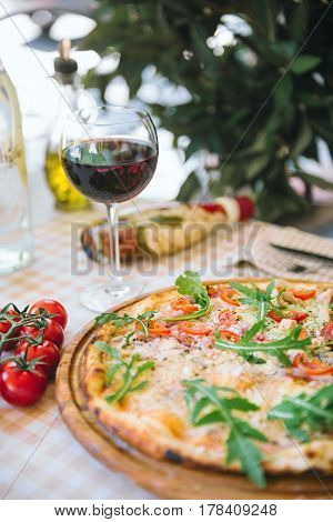 Pizza with cheese, tomato and meat, with glass of wine on served table with plaid tablecloth