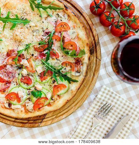 Pizza with cheese, tomato and meat, with glass of wine on served table with plaid tablecloth