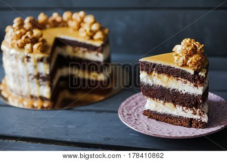 Delicious cake with caramel popcorn and caramel sauce and plate with slace of this cake