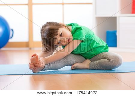 cute little girl stretching on mat in gym