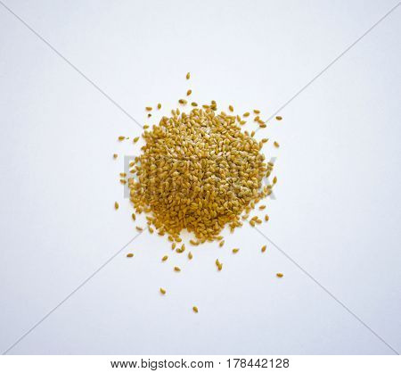 Spilled pile of golden flax seeds are isolated on a white background