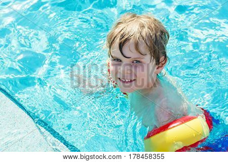 happy little kid boy having fun in an swimming pool. active happy child learning to swim. with safe floaties or swimmies. family, vacations, summer concept.