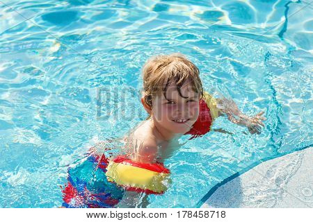 happy little kid boy having fun in an swimming pool. active happy child learning to swim. with safe floaties or swimmies. family, vacations, summer concept.