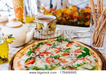 Pizza with cheese, tomato and meat, with cup of tee on served table with plaid tablecloth