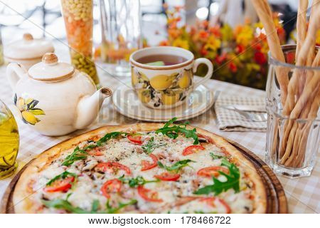 Pizza with cheese, tomato and meat, with cup of tee on served table with plaid tablecloth