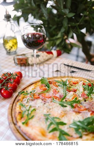Pizza with cheese, tomato and meat, with glass of wine on served table with plaid tablecloth