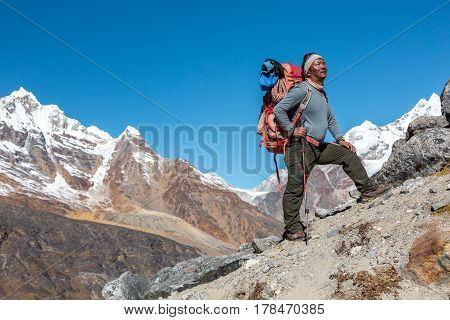Mature high Altitude Himalaya Nepalese Mountain Guide staying on rocky Slope with Backpack Climbing Gear and looking Up