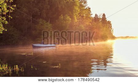 A young guy rides a boat on a lake during a golden sunset. Man rowing a boat in backlight of the sun. Unity with nature concept