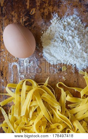 Fresh uncooked homemade noodles with ingredients egg and flour on rustic wooden table. Top view.