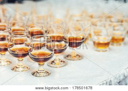 Row of glasses with whiskey or cognac on the table. Strong alcohol in a bar or restaurant. Transparent glasses with an alcoholic drink