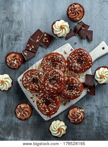 donut rings and vanilla caramel cupcakes with white and dark chocolate chippings and icing served on board.