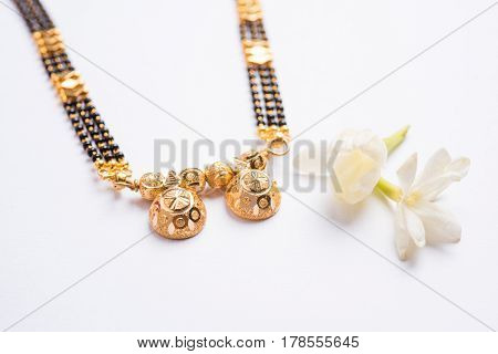close-up photo of a Mangalsutra or necklace to worn by a married hindu women, with huldi kumkum and mogra flowers or Jasminum sambac garland over white background