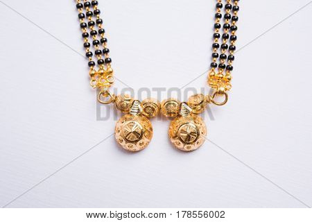 close-up photo of a Mangalsutra or necklace to worn by a married hindu women, with huldi kumkum and mogra flowers or Jasminum sambac garland over white background