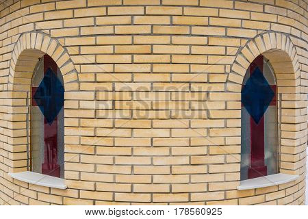 Closeup of round beige brick wall of a chirch with arched windows with image of cross