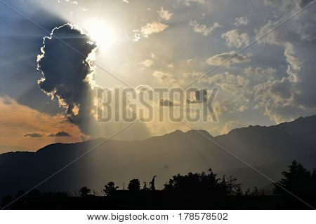 Sun-rays trying to escape a dark cloud in a hilly area.