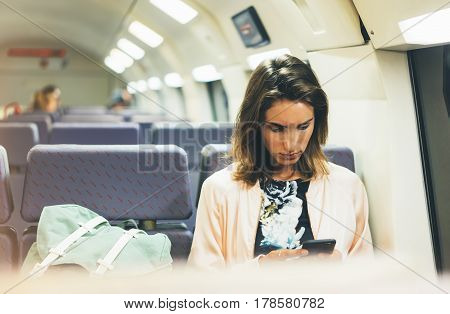 Enjoying travel. Young pretty woman traveling by train sitting near the window using smartphone and looking map in nigth. Tourist texting online message and plan route of railway railroad transport concept