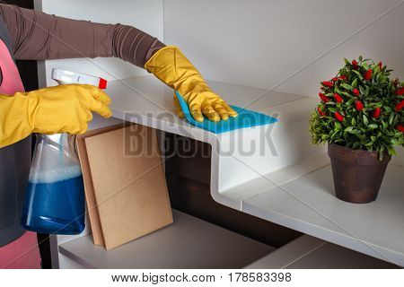 Female hands in gloves cleans the shelf with spray