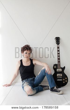 the girl with the guitar sits on the floor jeans shoes