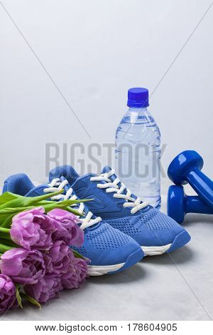 Spring sport composition with blue sneakers dumbbells bottle of water and purple tulips on gray concrete background. Concept healthy lifestyle sport and diet in spring. Place for copyspace.