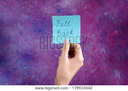 Female hand holding card with text FALL BACK on color background