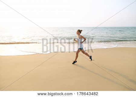 Young woman is jogging during the sunrise on beach