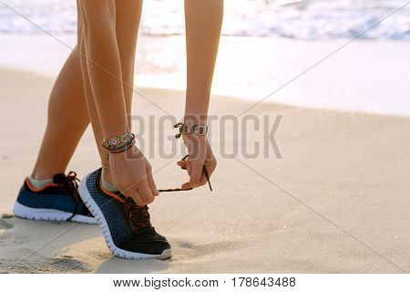 Healthy runner woman tying running shoes laces getting ready for beach jogging. Female athlete living a fit and active life