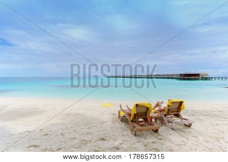 Tourists sunbathing and reading book on the beach in tropical Maldives island