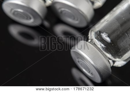 Medical injection vials with clear liquid. The bottles are lying down in a clear black background with reflection