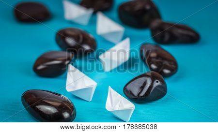 White paper boats in sigle file between abstract rock stones on blue background.