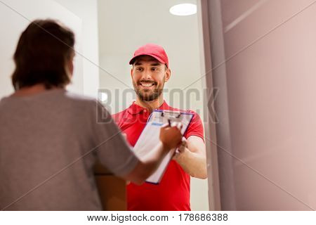 delivery, mail, people and shipping concept - happy man delivering parcel boxes and customer signing form on clipboard at home