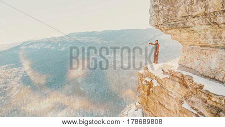 Explorer young man standing on high cliff Eagle shelf and pointing into the distance in winter Mezmay Russia. Image with sunlight effect.