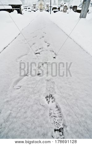 Foot steps in snow in cemetery and winter catholic church. Religious graveyard with tomb stones and a church in snowy winter and foot tracks made with boots or shoes.