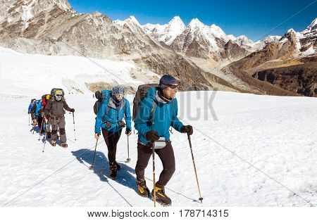 Group of Mountain climbers led by serious mature Guide in weather protective Clothing walking up on snowy Glacier, Scenery of high Peaks and Summits on Background warm tones