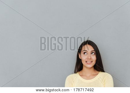 Image of thoughtful woman dressed in yellow sweater posing over grey wall and looking aside to copyspace