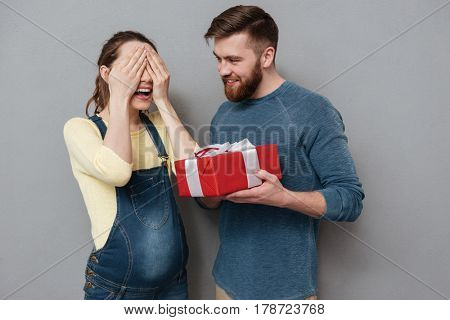 Happy pregnant woman with eyes closed taking gift from her husband isolated