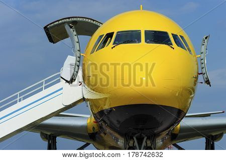 Yellow passenger plane with opened door and ramp near entrance in airplane, aviation and aerospace industry, blue sky on background