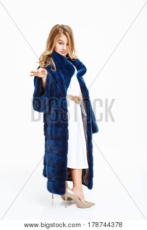 Girl in long fur coat, white midi dress, beige heels shoes posing with hand up.