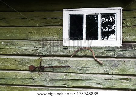 Conceptual photography: wooden wall of an old house with ancient agricultural working tools and the window. Village life in detail. Hammer iron adorns the building.