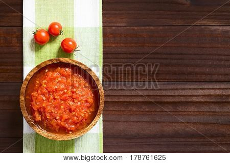 Homemade traditional Italian marinara or pomodoro tomato sauce made of fresh tomato garlic dried oregano and salt served in wooden bowl with cherry tomatoes on the side photographed overhead on dark wood with natural light