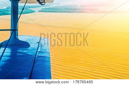 A view of the wing of a turboprop aircraft and a field of corn and wheat in the countryside.