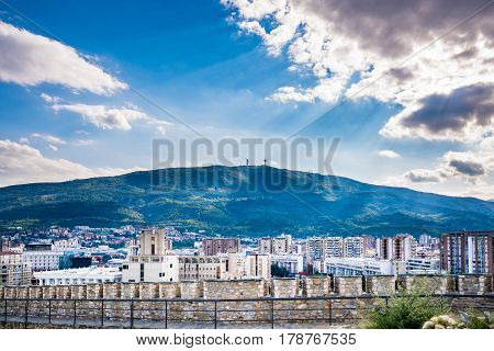 Dramatic and beautiful city landscape view of the city Skopje in Macedonia with the mountain Vodno in the background. Sun rays shining through the clouds.