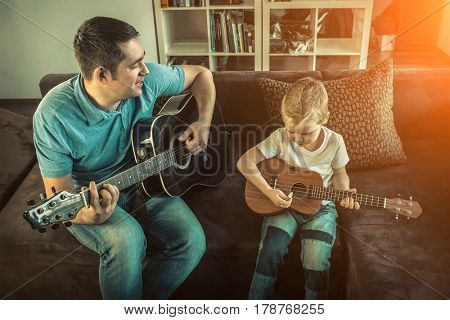 Father teaching his son to play on guitar at home. Son play on ukulele - hawaiian guitar.