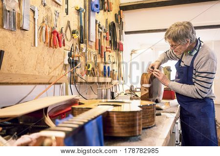 Luthier - instrument maker - applying masking tape to an old acoustic guitar body with another guitar in the foreground