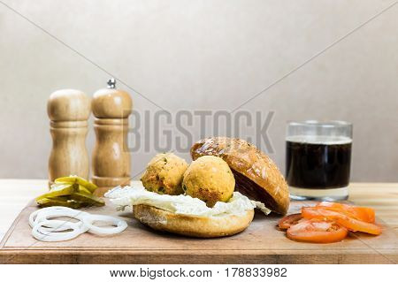 Vegan burger ingredients on wood table. Vegetables, vegan ball cutlets made of chick peas soft drink on cutting board ready to be put into vegetarian hamburger